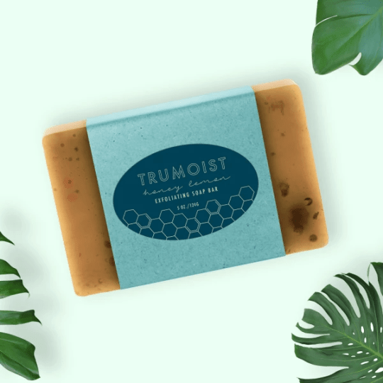 "Trumoist" mézes-citromos hámlasztó szappan kék papírpántban, monstera levelek hátterével.
