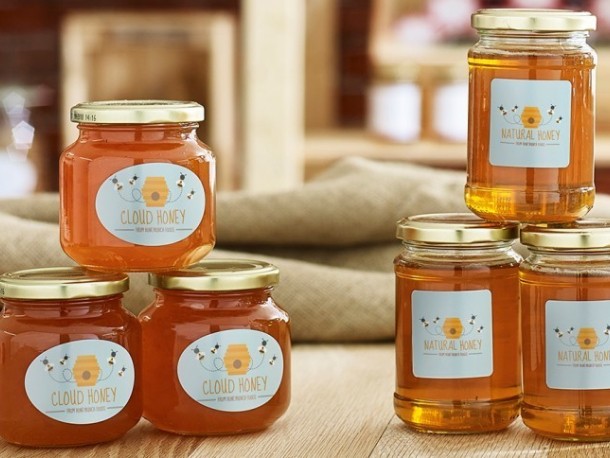 Hat üveg méz egy fa asztalon. A címkéken "Cloud Honey" és "Natural Honey" feliratok, valamint egy méhkast és méheket ábrázoló grafika látható.