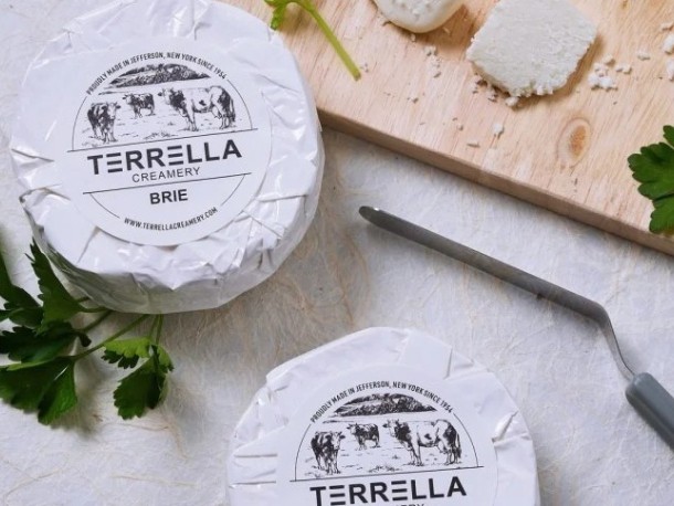 Két Terella Creamery Brie sajt csomag egy vágódeszkán, sajtkéssel és petrezselyemmel.