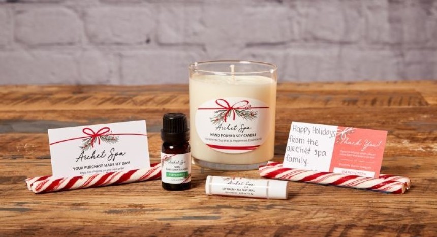 Asztalon elrendezett karácsonyi ajándékcsomag: szója gyertya, illóolaj, ajakbalzsam és cukorpálca, köszönőkártyákkal.