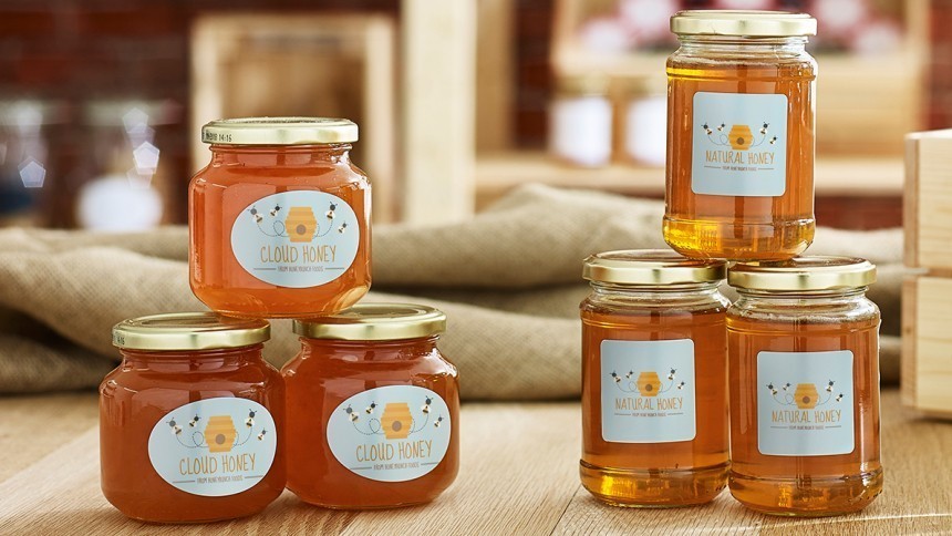 Hat üveg méz egy fa asztalon. A címkéken "Cloud Honey" és "Natural Honey" feliratok, valamint egy méhkast és méheket ábrázoló grafika látható.