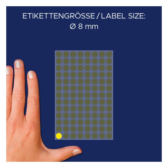 A képen látható egy kéz egy 8 mm átmérőjű kör alakú címkéket tartalmazó lap mellett. A címkék többsége szürke, az alsó bal sarokban pedig egy sárga címke található. A háttér sötét kék.