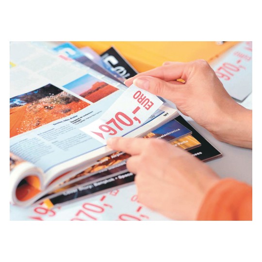 A close-up of a person's hand flipping through a colorful magazine, showcasing an image of a red landscape and a price tag marked €970.