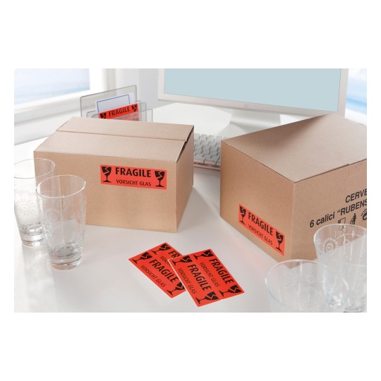 The image shows two cardboard boxes labeled 'Fragile' with glassware nearby. There are glass tumblers on the table and several warning labels indicating fragility.