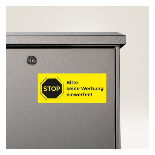 A képen egy postaláda közelről látható, amelyen egy élénksárga matrica található a következő felirattal: 'STOP bitte keine Werbung einwerfen!', ami azt jelzi, hogy ne dobjanak be reklámanyagokat.