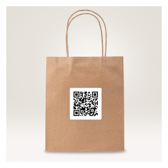 A kép egy barna papírzacskót mutat, amelyen egy QR-kód matrica található. A zacskón két csavart papírfogantyú van, és világos háttér előtt van elhelyezve.