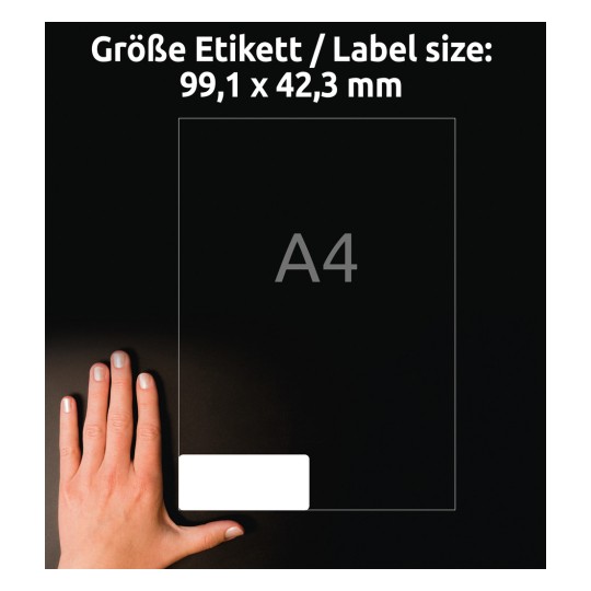 A képen egy kéz látható a méretarányt jelző címke mellett, amelynek méretei 99,1 x 42,3 mm. A címke egy A4 méretű kereten belül van meghatározva sötét háttér előtt.