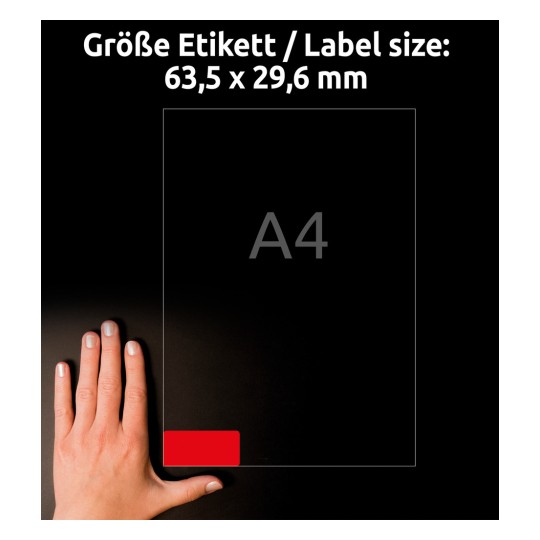 A kép egy kéz és egy A4 méretű címkelap mellé helyezett kézfejét mutatja, 63,5 x 29,6 mm-es méretekkel, amelyek fent vannak feltüntetve. Egy piros címke van kiemelve az alsó sarokban.