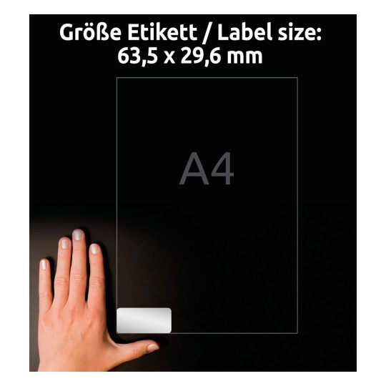 A kép egy kezet ábrázol, amely egy átlátszó címkét tart, rajta a címke mérete: 63,5 x 29,6 mm, mellette egy A4-es papírméret referenciával.