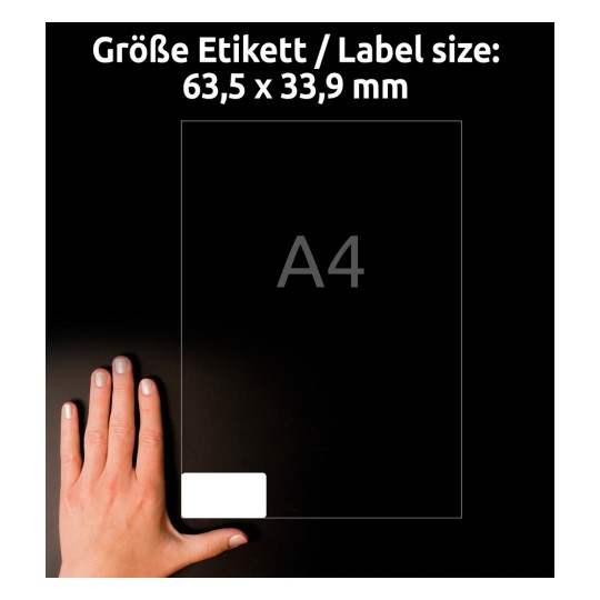 A képen egy kéz látható, amely egy 'A4' jelölésű átlátszó lapot tart, amelyen a címke mérete 63,5 x 33,9 mm. A háttér sötét, kiemelve a lapot.