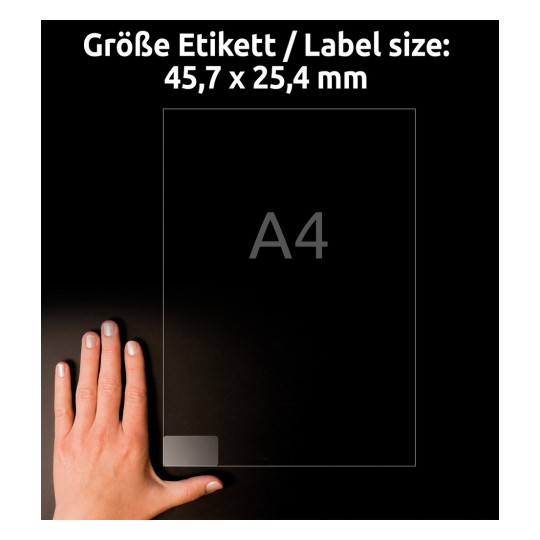 A kép egy kézben tartott címkét vagy dokumentumot ábrázol, amelynek méretei 45,7 x 25,4 mm, az A4-es papírméret mellett, sötét háttér előtt.