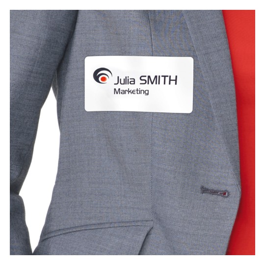 A képen egy személy látható, aki szürke zakót visel, melyen egy névtábla van, amin a következő felirat olvasható: 'Julia SMITH Marketing'.