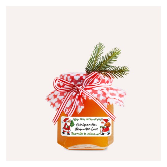 A képen egy házi készítésű karácsonyi dzsem látható, amelyet piros-fehér mintás fedéllel és dekoratív szalaggal díszítettek. Egy kis zöld fenyőág van ráhelyezve, ami ünnepi hangulatot kölcsönöz.