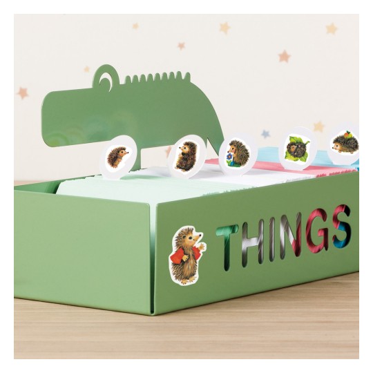 A kép egy zöld dobozt ábrázol, amelyen a "THINGS" felirat szerepel és egy dinoszaurusz fej dizájn látható a tetején. Belül színes kártyák vannak, és elöl, valamint felül több sün matricával van díszítve.