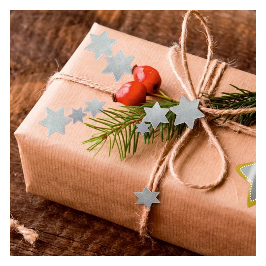 A képen egy szépen becsomagolt ajándék látható barna papírban, természetes zsineg masnival, zöld levelekkel, piros bogyókkal és kék csillag alakú kivágásokkal díszítve.