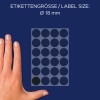 A képen egy kéz látható, amely egy címkelapot tart kör alakú címkékkel, amelyek átmérője 18 mm. A háttér sötétkék, és különböző kör alakú címkék láthatók rácsos elrendezésben, amelyek közül az egyik címke feketének tűnik.