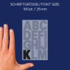 A képen egy kéz látható egy kártya mellett, amelyen az A-tól M-ig terjedő nagybetűk szerepelnek 100 pt (25 mm) betűmérettel. A 'K' betű fekete színnel van kiemelve egy világosabb háttér előtt, míg a többi betű világosabb árnyalatú.