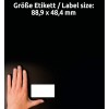 A kép egy sötét háttér előtt egy kézzel szemben elhelyezkedő üres címkét mutat. A címke méreteit németül említik, 88,9 x 48,4 mm-ként.