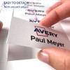 A képen egy kéz látható, amint egy címkét választ le egy ívről, amelyen a 'Paul Meyer' név és az 'Avery' logó szerepel, valamint egy megjegyzés, amely jelzi, hogy könnyű leválasztani, sima szélekkel.