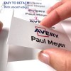 A kép egy kártyát tartó kezet mutat, amelyen az 'Avery' és 'Paul Meyer' feliratok vannak, jelezve, hogy könnyen leválasztható sima szélekkel. Több kártya látható a háttérben.