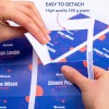 A kép kezeket mutat, amint egy szakaszt választanak le egy kiváló minőségű nyomtatott papírról, amelyen nevek és szerepkörök láthatók. A háttér élénk dizájnnal rendelkezik, kék és piros elemekkel.