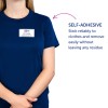 A képen egy sötétkék pólót viselő személy látható, akinek az öntapadós névcímkéjén az áll: 'B. Carlos, Marketingigazgató'. Mellette egy leírás található, amely kiemeli a névcímke öntapadós jellegét, hangsúlyozva annak megbízhatóságát és könnyű eltávolíthatóságát maradvány nélkül.