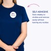 A képen egy személy látható, aki egy kék pólót visel, amelyen egy öntapadós névcímke található 'B. Carlos, Marketing Igazgató' felirattal. A szöveg kiemeli, hogy a címke megbízhatóan tapad a ruhára, és könnyen eltávolítható, maradványok nélkül.