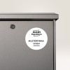 A képen egy szürke fém tárgy közelképe látható, amelyen kulcslyuk és egy kör alakú címke van. A címkén az 'AVERY Zweckform MUSTERFIRMA GmbH' szöveg szerepel, ami arra utal, hogy ez egy tárolóegység vagy szekrény lehet.