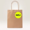 A kép egy barna papír bevásárlótáskát ábrázol, amelyen egy kör alakú, neonsárga címke található fekete betűkkel a "NEU" felirattal.