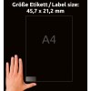 A képen egy kéz látható, amely egy 'A4' feliratú átlátszó lapot tart, rajta a méretek németül vannak feltüntetve: 'Größe Etikett / Label size: 45,7 x 21,2 mm'. A háttér fekete.