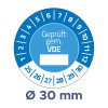 A képen egy kerek mérőeszköz vagy címke látható kék és fehér mintával. A közepén a „Geprüft gem. VDE” szöveg található, amelyet 1-től 30-ig számozott jelölések vesznek körül. A címke továbbá egy 'Ø 30 mm' átmérőt is jelez.