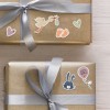 A kép két gyönyörűen csomagolt, aranyszínű ajándékot mutat. A dobozokat játékos matricák díszítik, többek között egy gólyát, babatalpakat, szíveket, egy nyulat és egy „girl” feliratú lufit. Az ajándékokat egy ezüst szalag köti össze, ami ünnepi hangulatot kölcsönöz.