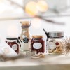 A képen házi készítésű befőtteket és süteményeket tartalmazó üvegek gyűjteménye látható, címkékkel és szalagokkal díszítve. Két üvegben lekvárok vannak, míg egy üveg tartályban kekszek találhatók. A környezet meleg, ünnepi hangulatú, lágy megvilágítással.