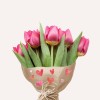 Egy csokor rózsaszín tulipán díszszívekkel ellátott papírba csomagolva, világos háttér előtt.